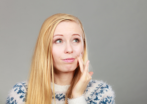 A woman in pain, looking off camera as she holds her left hand up to her jaw.