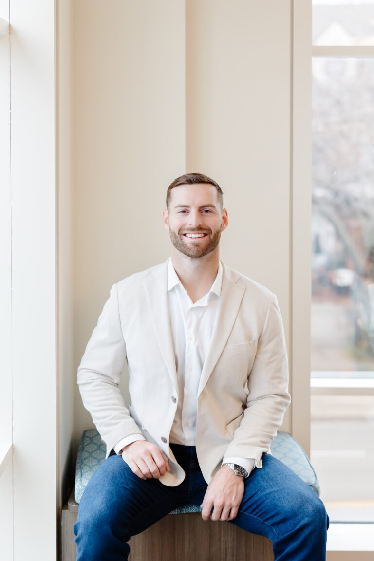 A headshot of Dr. Blake Bean in a white shirt and suit jacket standing in front of a white wall.
