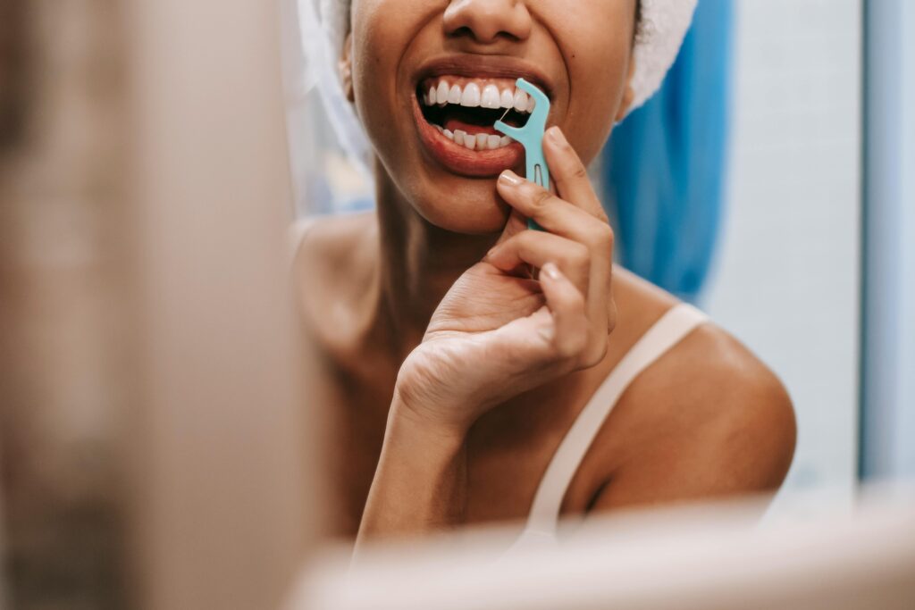 A woman pictured in her bathroom mirror using a floss pick to floss her upper teeth.