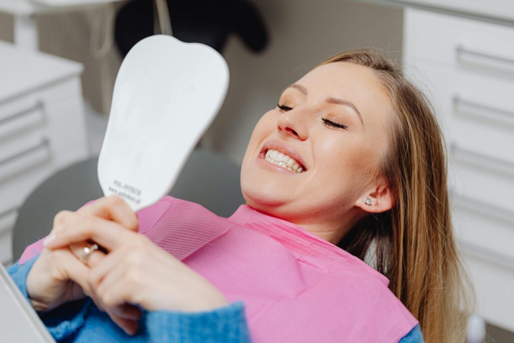 Woman checking her teeth in a handheld mirror at the dentist.