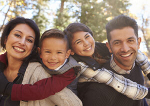 A family wearing fall clothing and smiling in the woods.