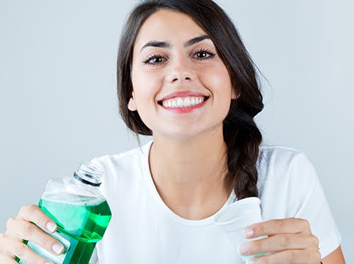 Woman holding mouthwash and smiling.