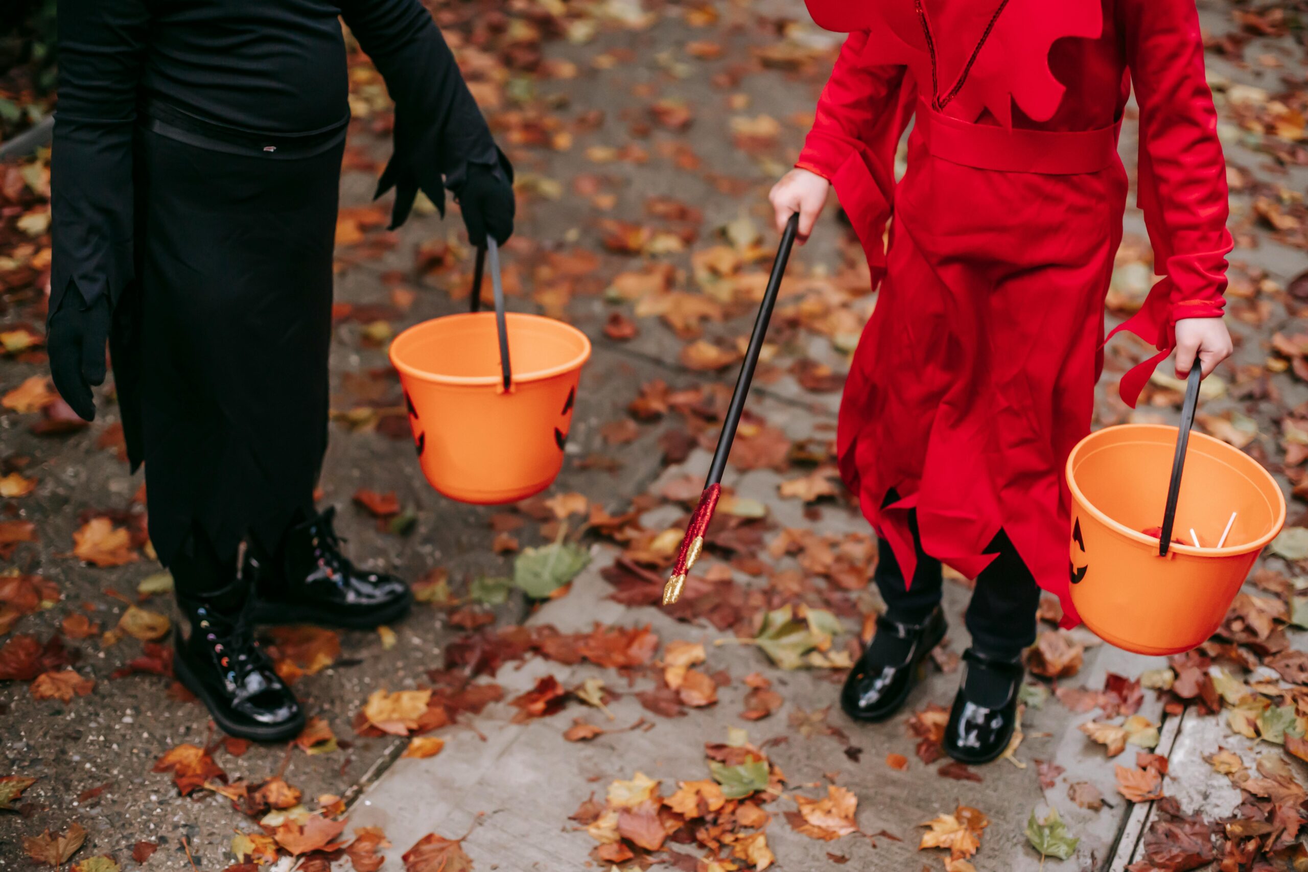 Kids dressed in costumes holding bright orange pumpkin buckets for candy, reminding families to plan ahead for safe trick-or-treating with braces.
