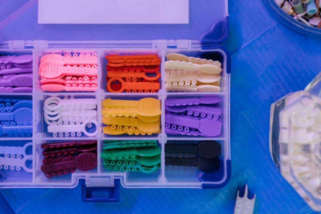A plastic organizer box is filled with rows of colorful orthodontic bands, also known as ligatures, used for braces.