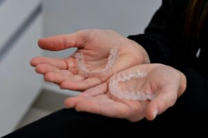 A pair of hands holds two clear dental aligners.