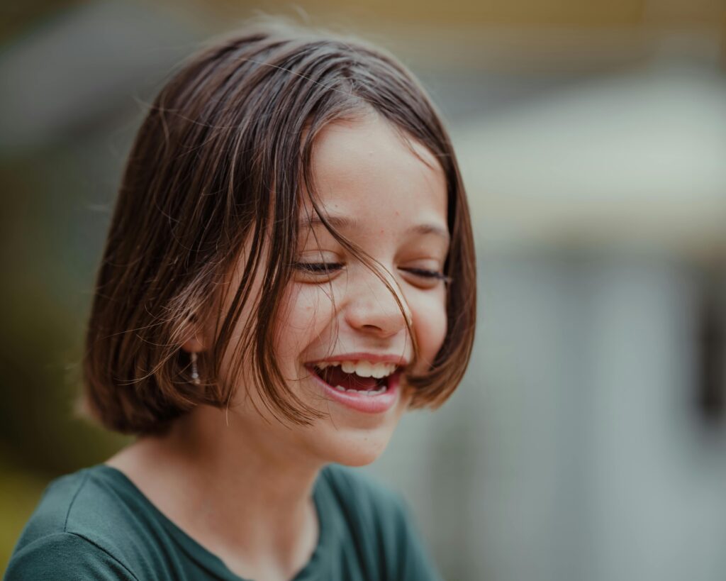 A happy child with short brown hair laughs with their eyes closed.